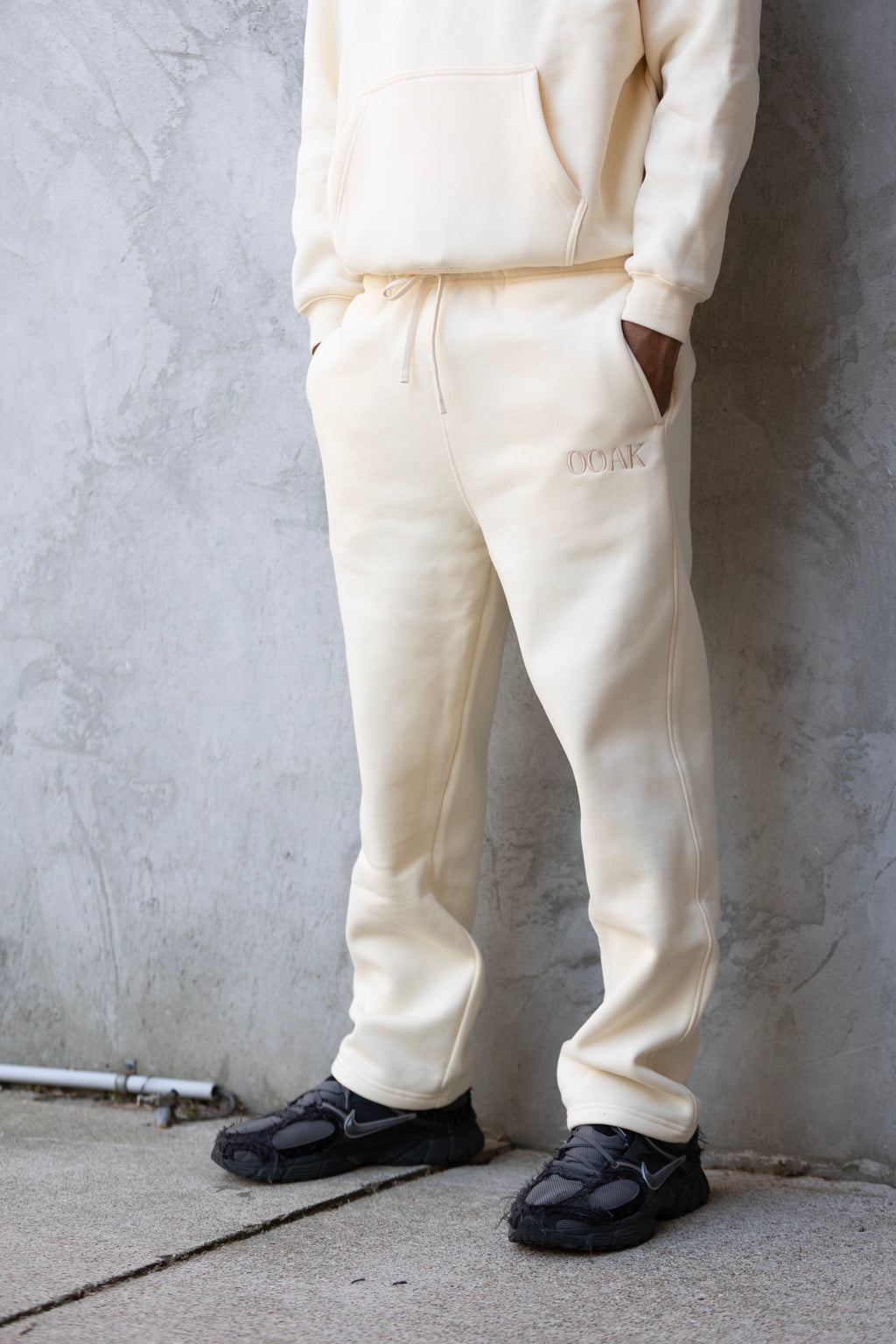 Person wearing a cream-colored hoodie and pants against a gray wall.