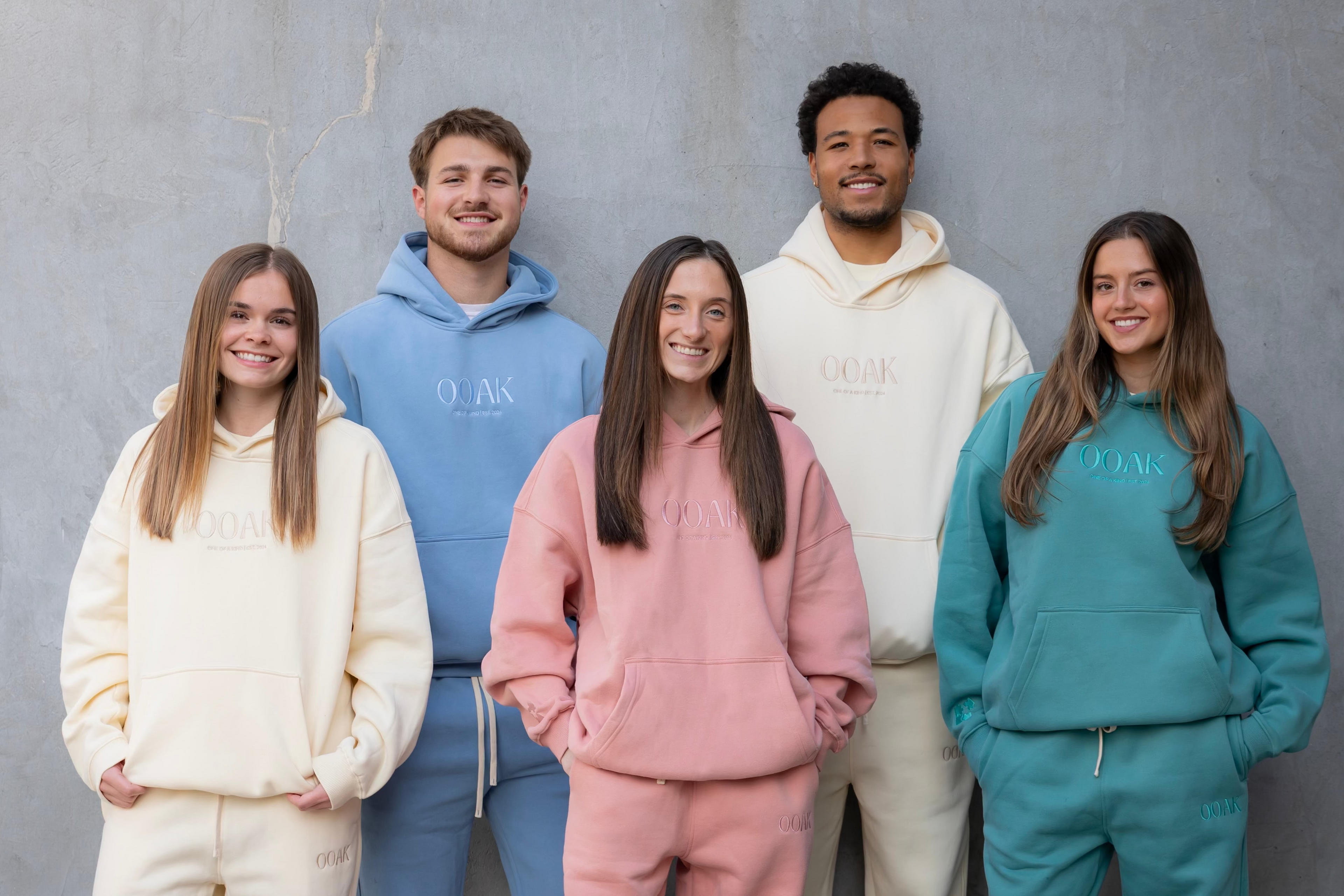 Five people wearing colorful hoodie and pants sets against a gray background