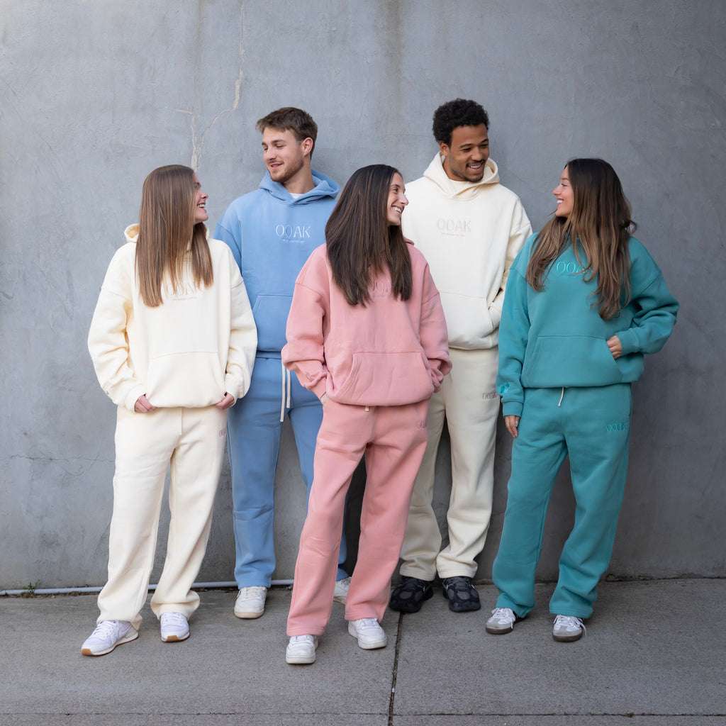 Five people wearing colorful tracksuits standing against a gray wall.
