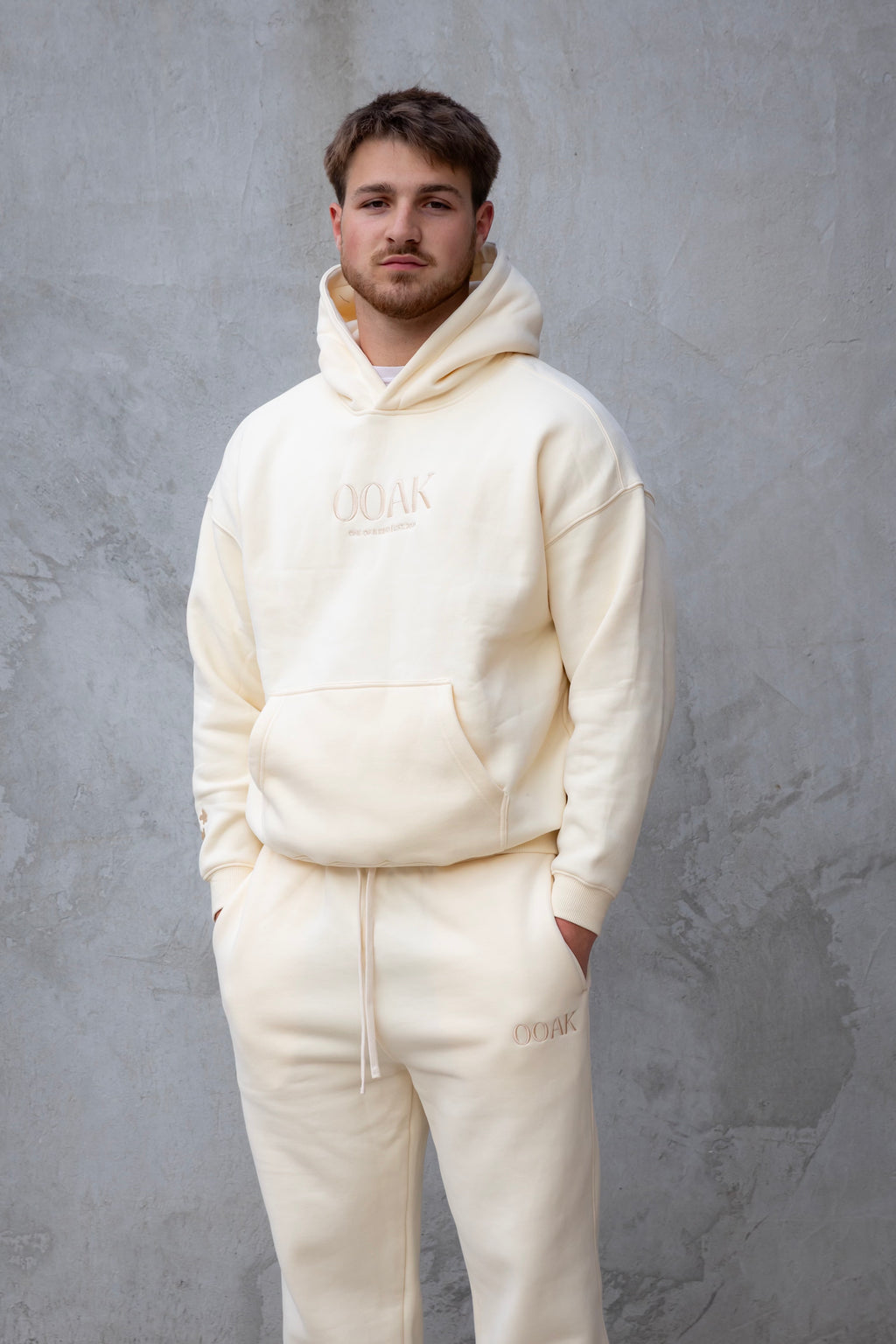 Man wearing a cream-colored hoodie and pants with 'OAMC' branding against a gray background