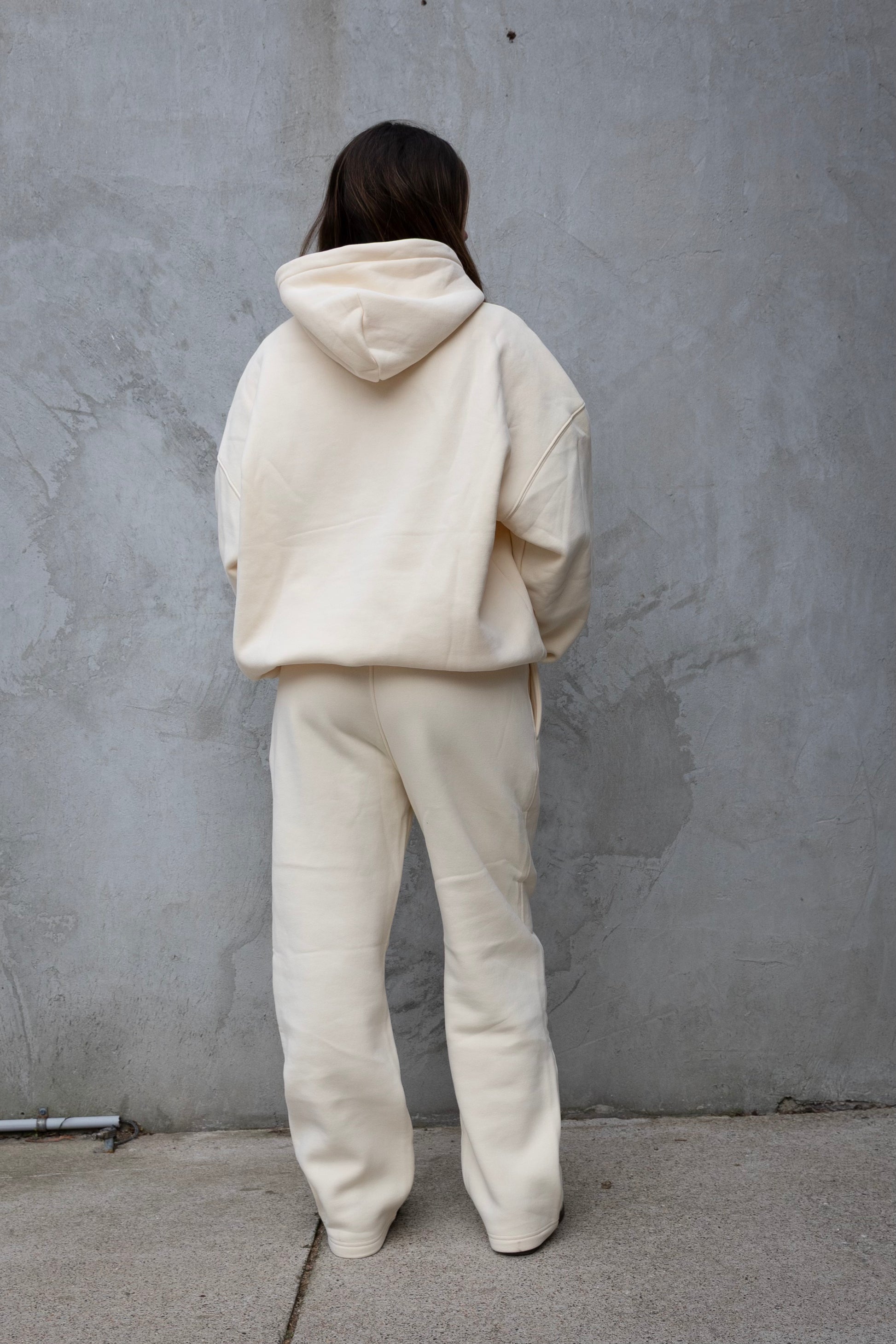 Person wearing a cream-colored hoodie and pants against a gray wall.