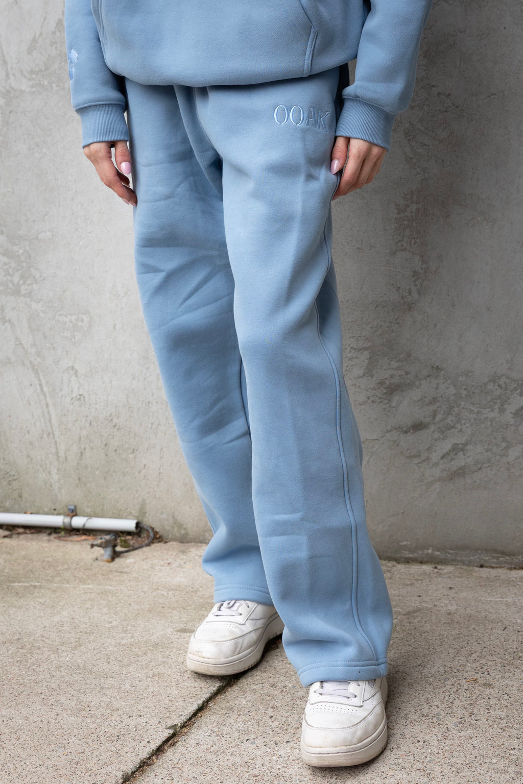 Person wearing a light blue tracksuit with 'OOAK' branding against a concrete wall.