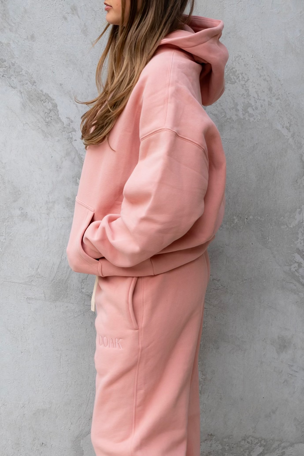 Person wearing a pink tracksuit standing against a gray wall.