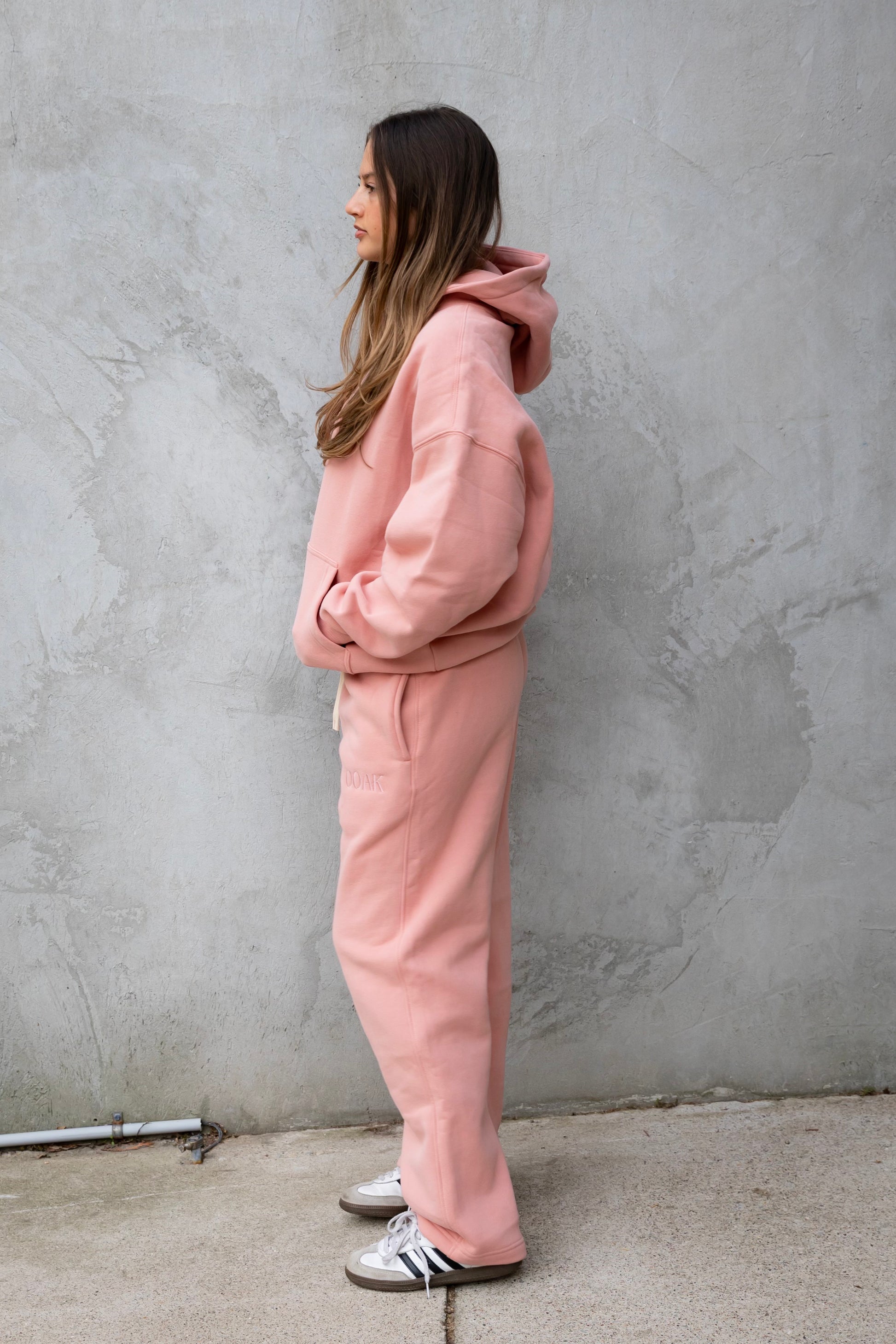 Person wearing a pink tracksuit standing against a gray wall.