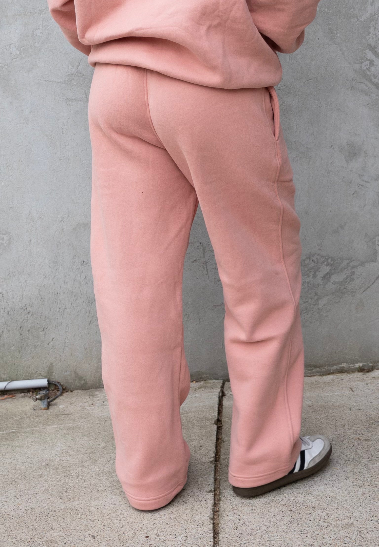 Person wearing pink sweatpants standing against a gray wall.