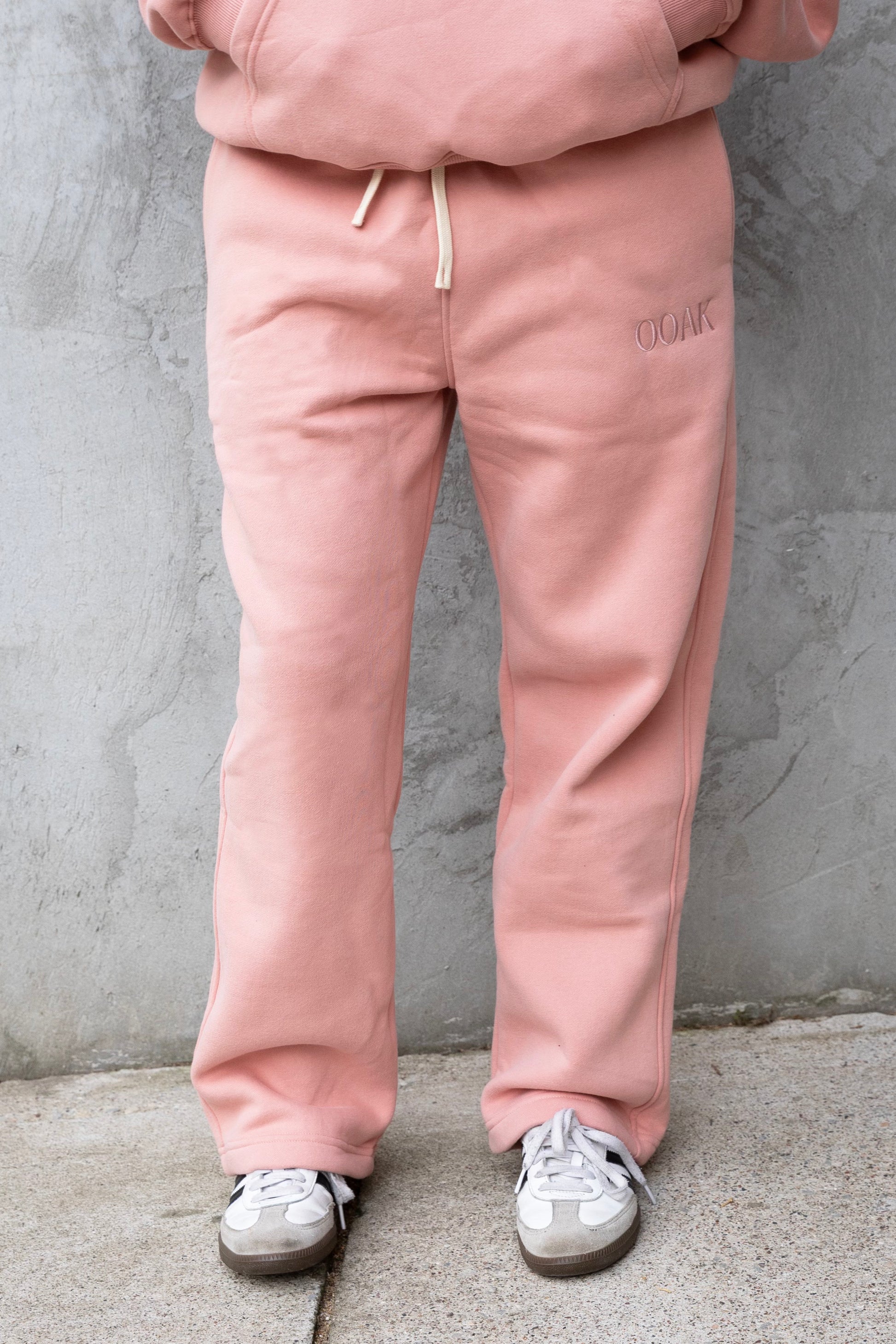 Person wearing a pink tracksuit with white sneakers against a gray concrete wall.