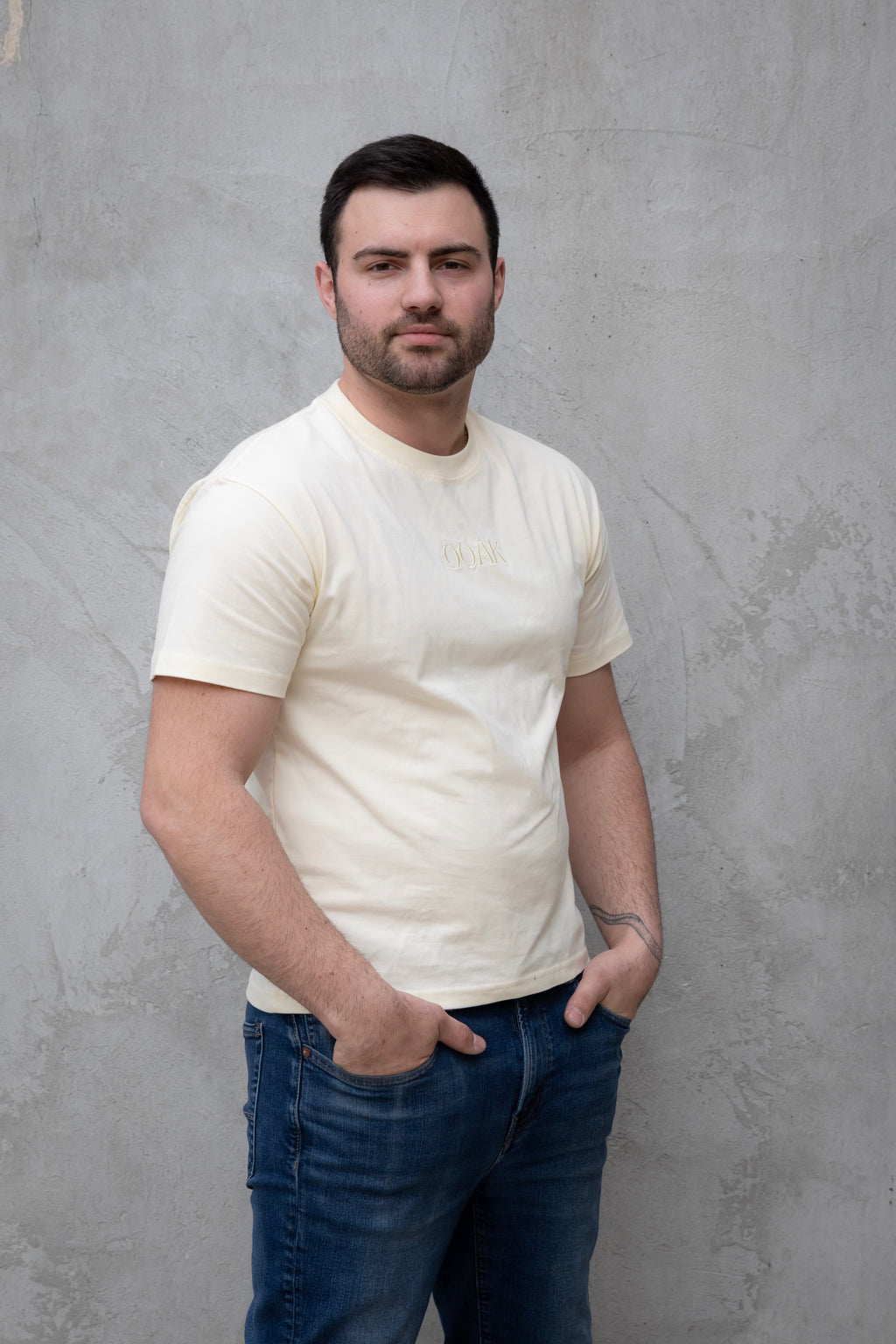 Man wearing a white t-shirt and blue jeans against a gray wall