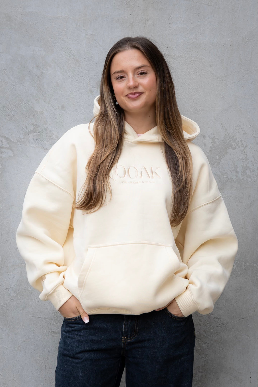 Woman wearing a cream hoodie with text on it against a gray background