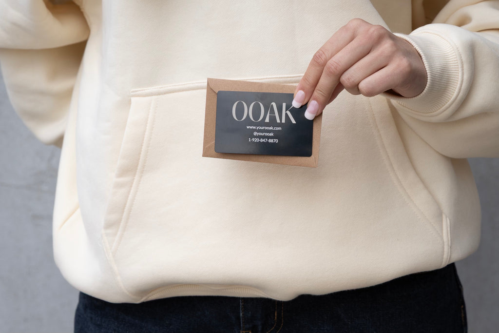 Person holding a 'OOAK' label on a beige hoodie against a gray background