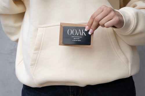 Person holding a 'OOAK' label on a beige hoodie against a gray background