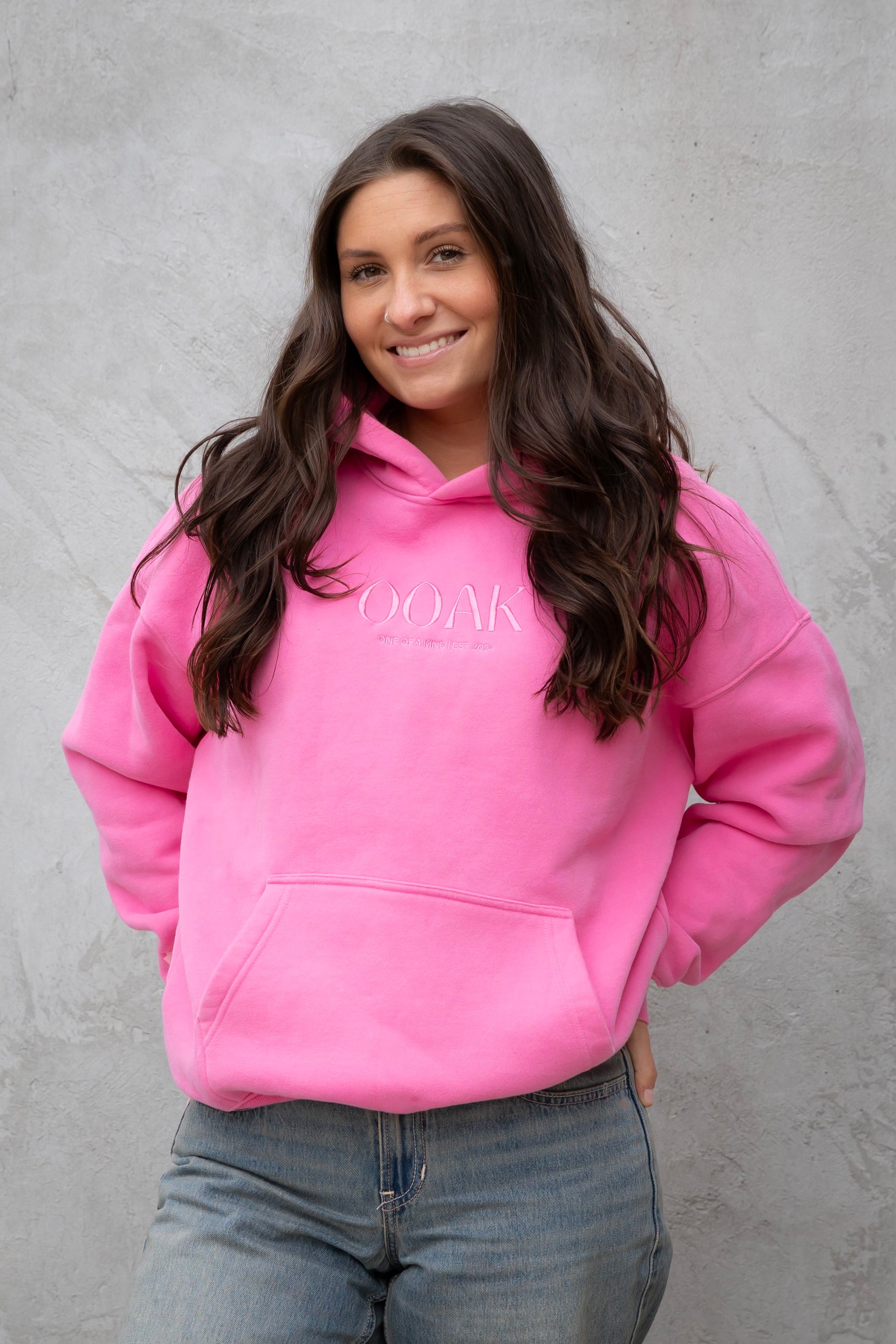 Person wearing a pink hoodie with text, standing against a gray background