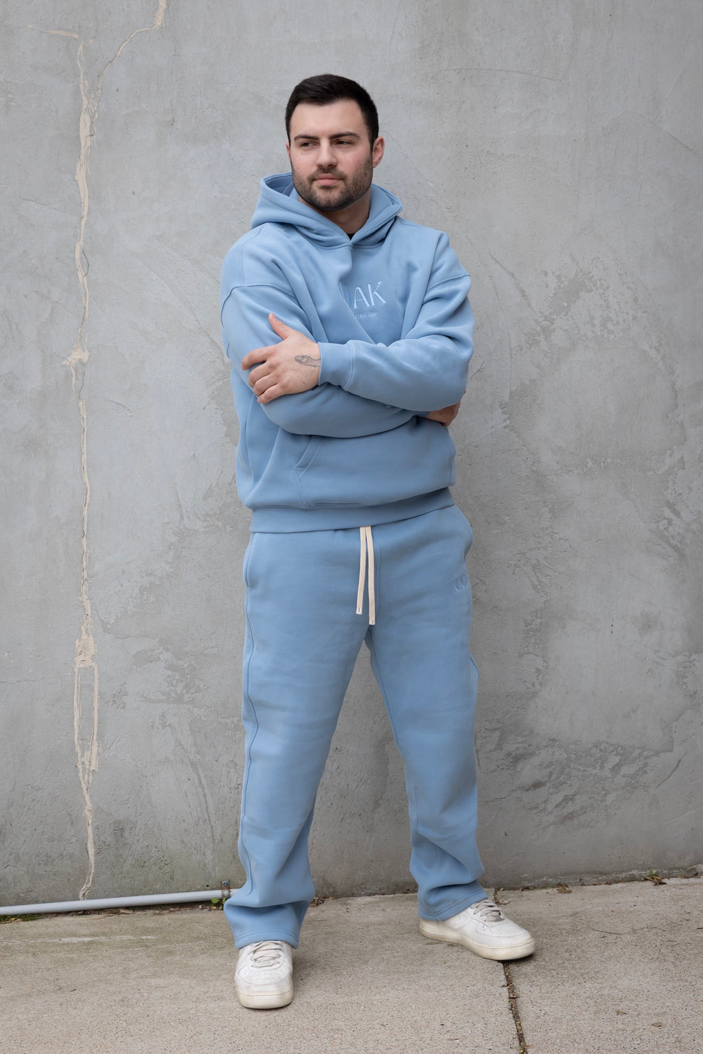 Man wearing a light blue tracksuit with a brand logo against a gray wall.