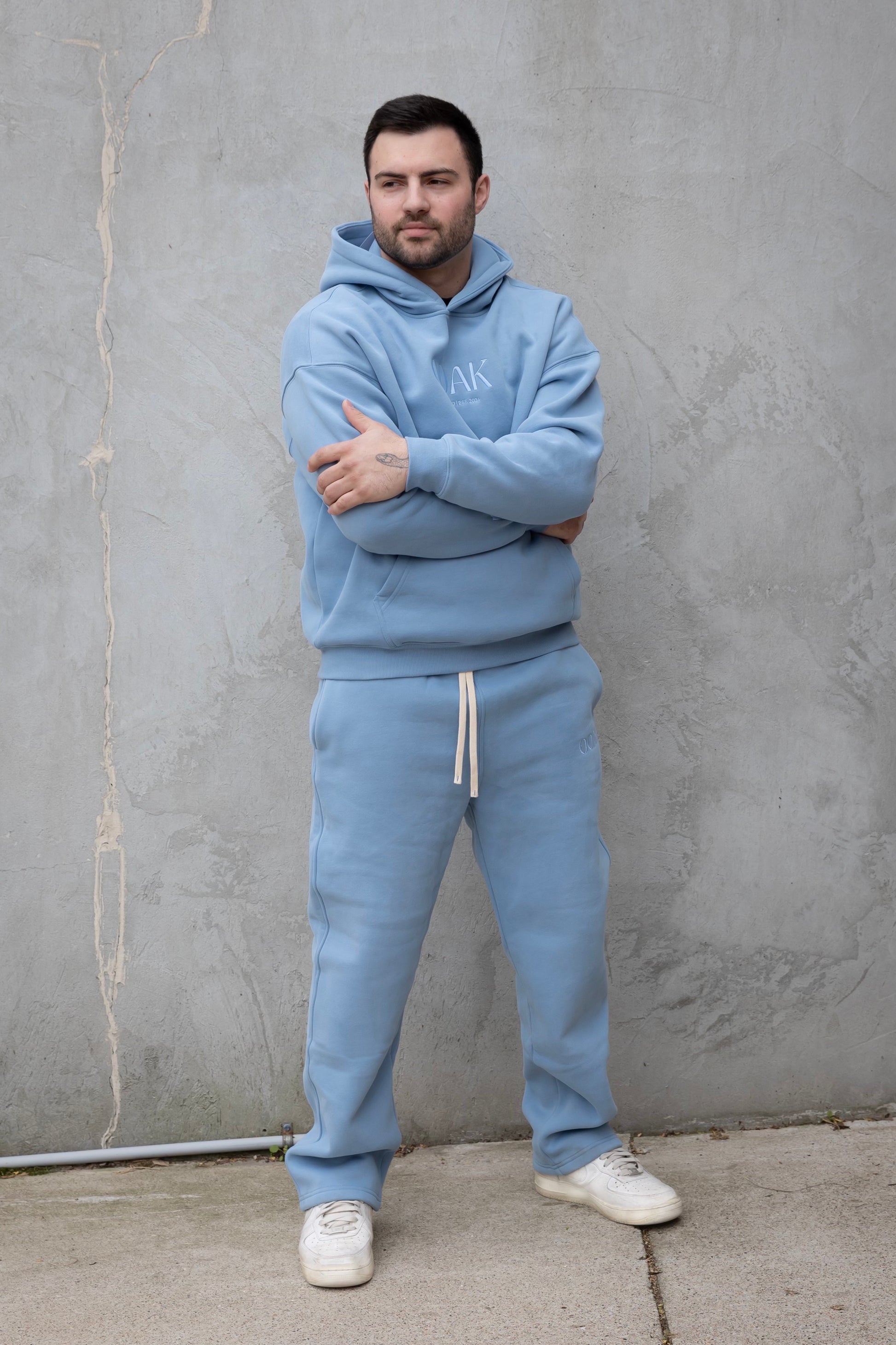 Man wearing a light blue tracksuit with a brand logo against a gray wall.