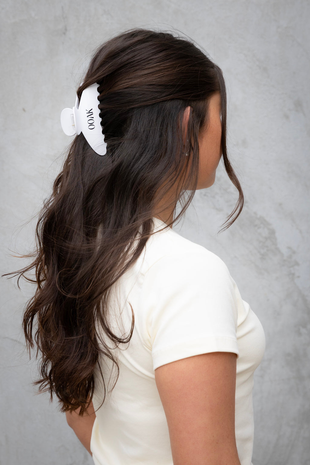 Person with long dark hair wearing a white hair clip against a gray background