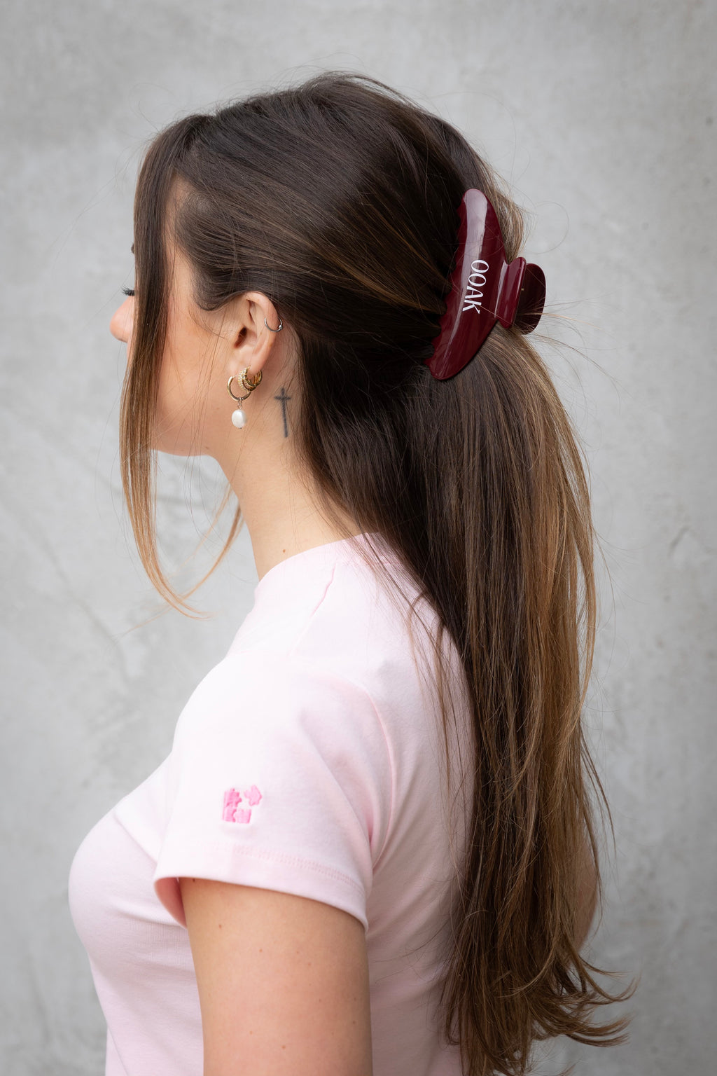 Woman with a hair clip and pink shirt against a gray background