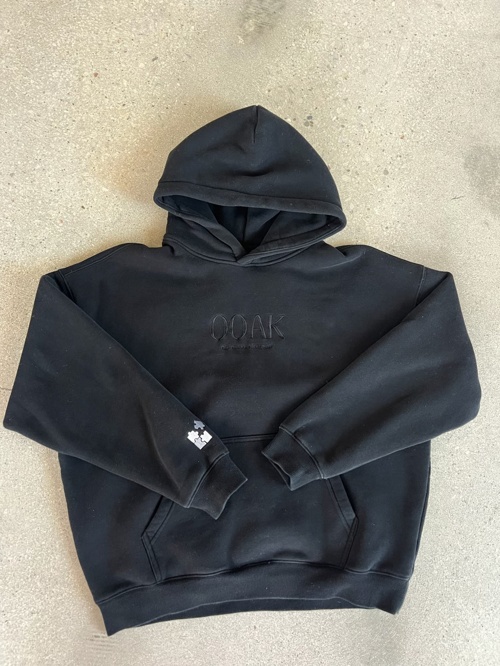 Black OOAK hoodie with a logo on a beige surface
