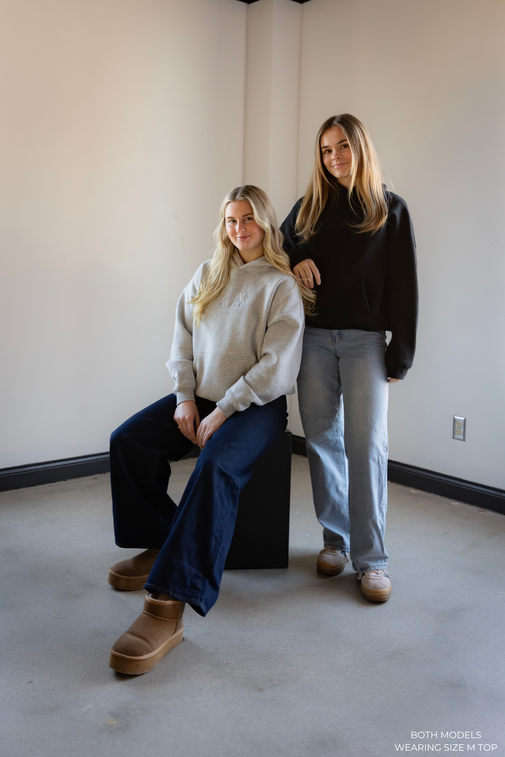 Two models standing in a minimalistic room wearing size M OOAK hoodies.