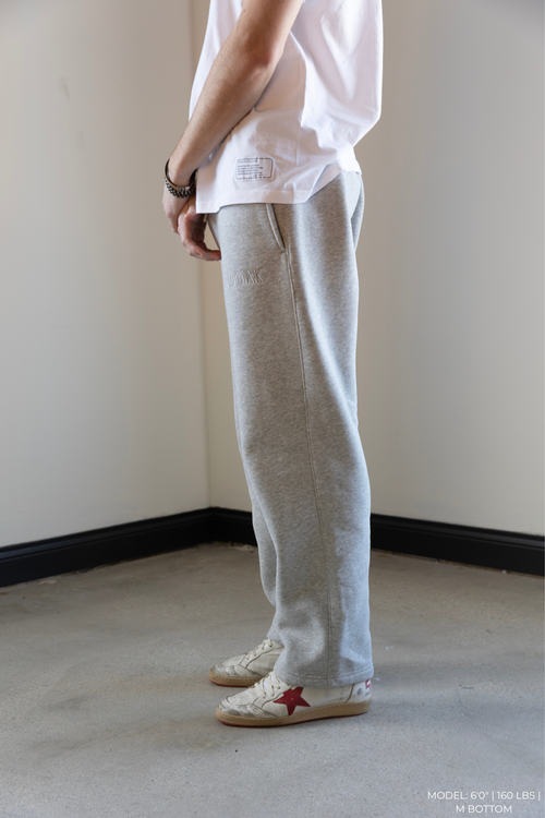 Person wearing a white OOAK shirt and gray OOAK sweatpants standing on a plain floor.