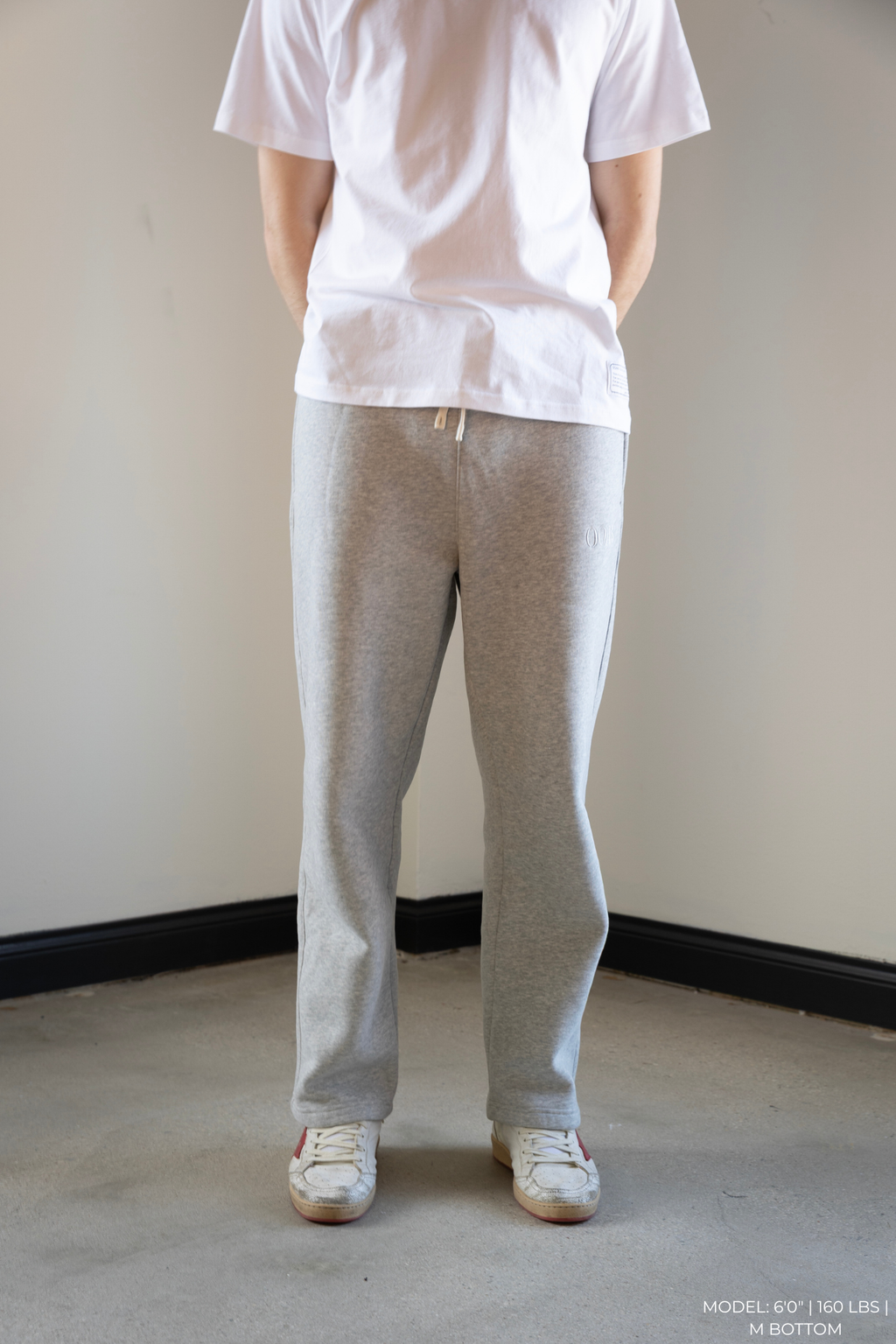 Person wearing a white OOAK t-shirt and gray OOAK sweatpants standing against a plain wall.