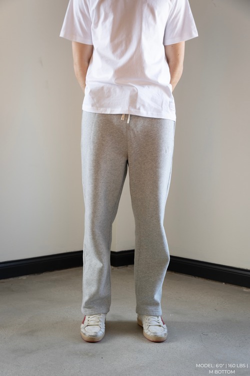 Person wearing a white OOAK t-shirt and gray OOAK sweatpants standing against a plain wall.