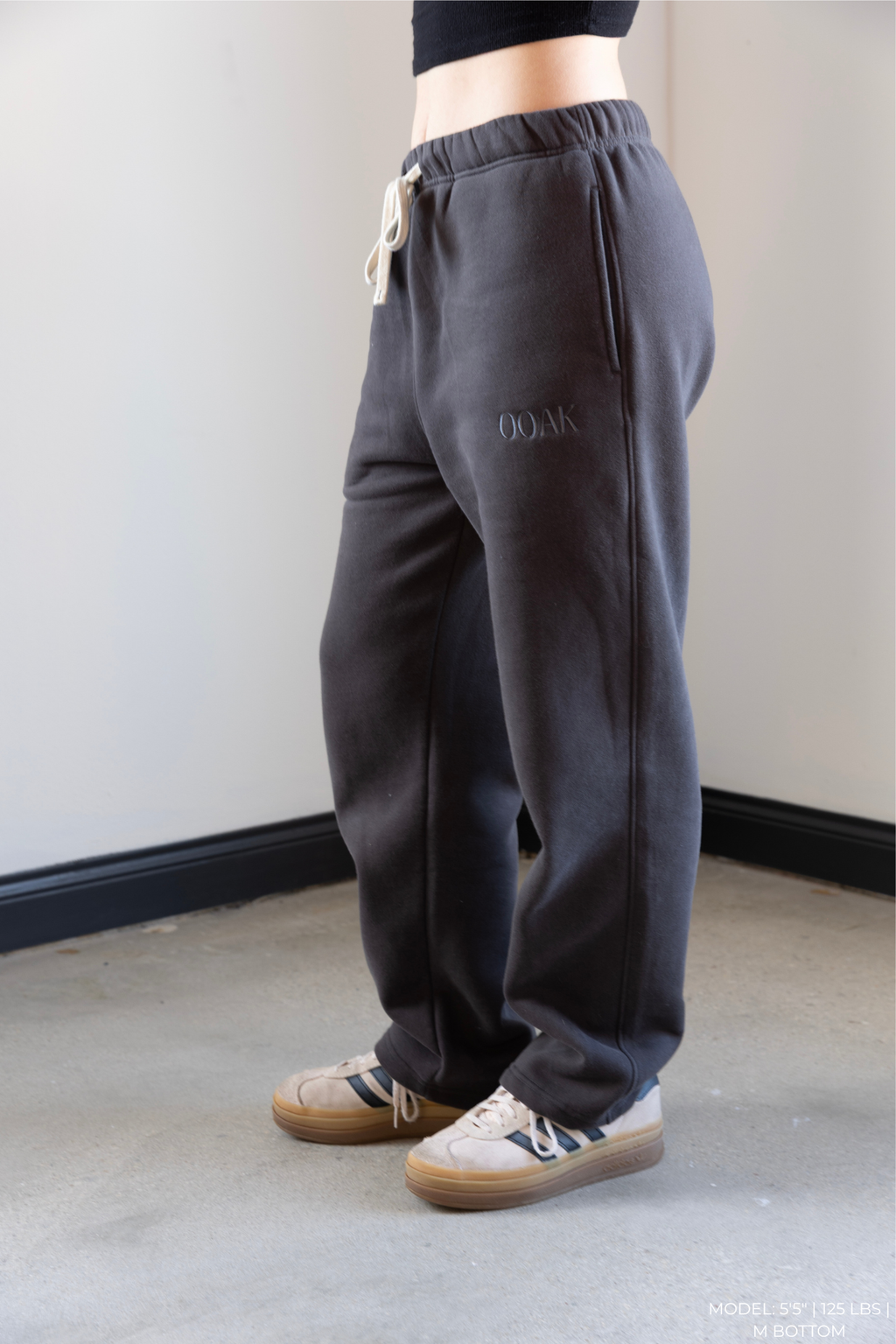 Model wearing dark gray OOAK sweatpants, standing against a plain wall.