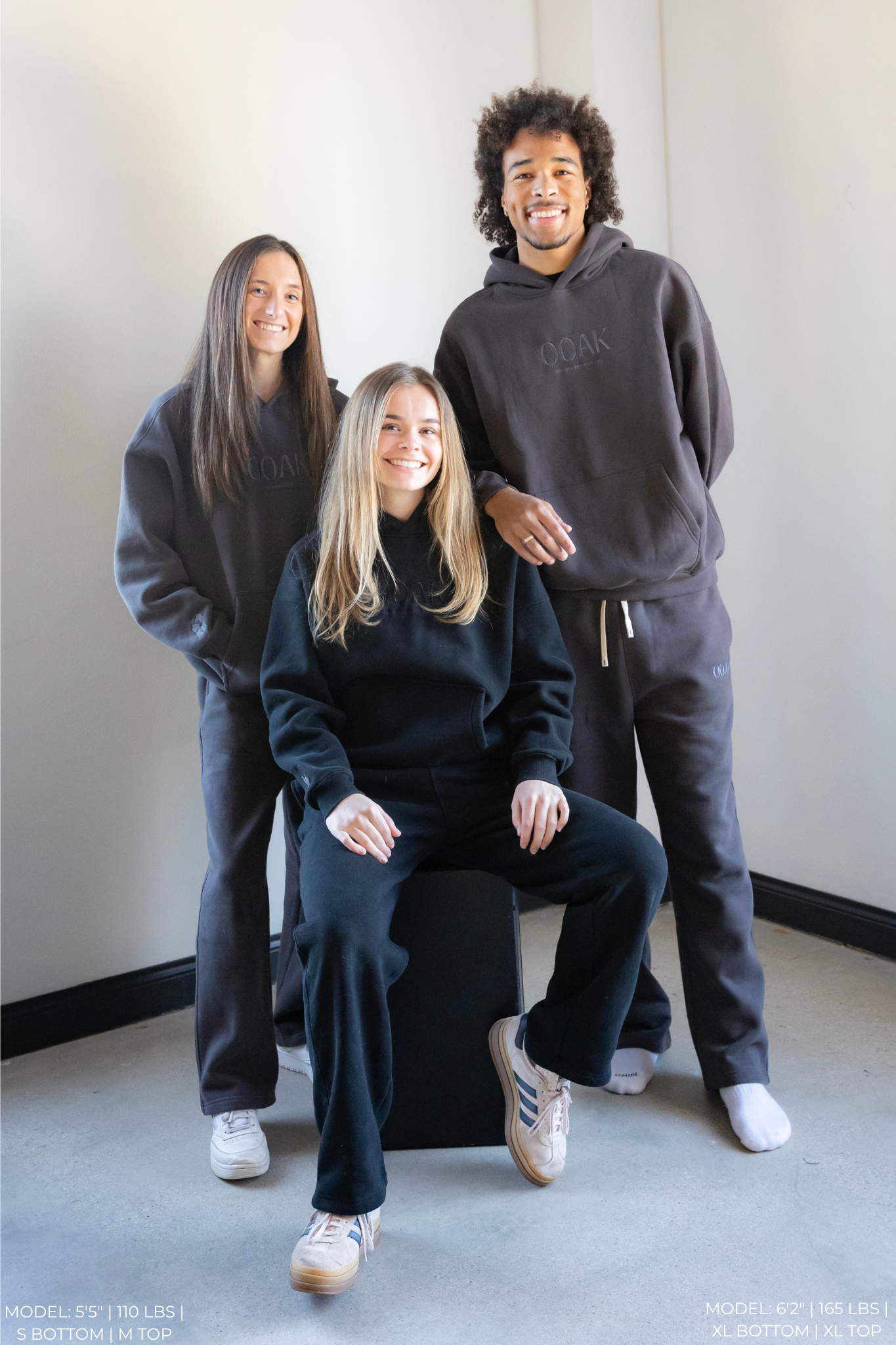Three people wearing matching dark gray OOAK sets in a minimalistic setting.
