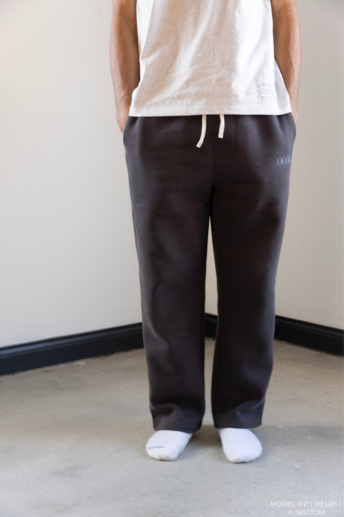 Person wearing dark gray OOAK sweatpants and a white top against a plain background.