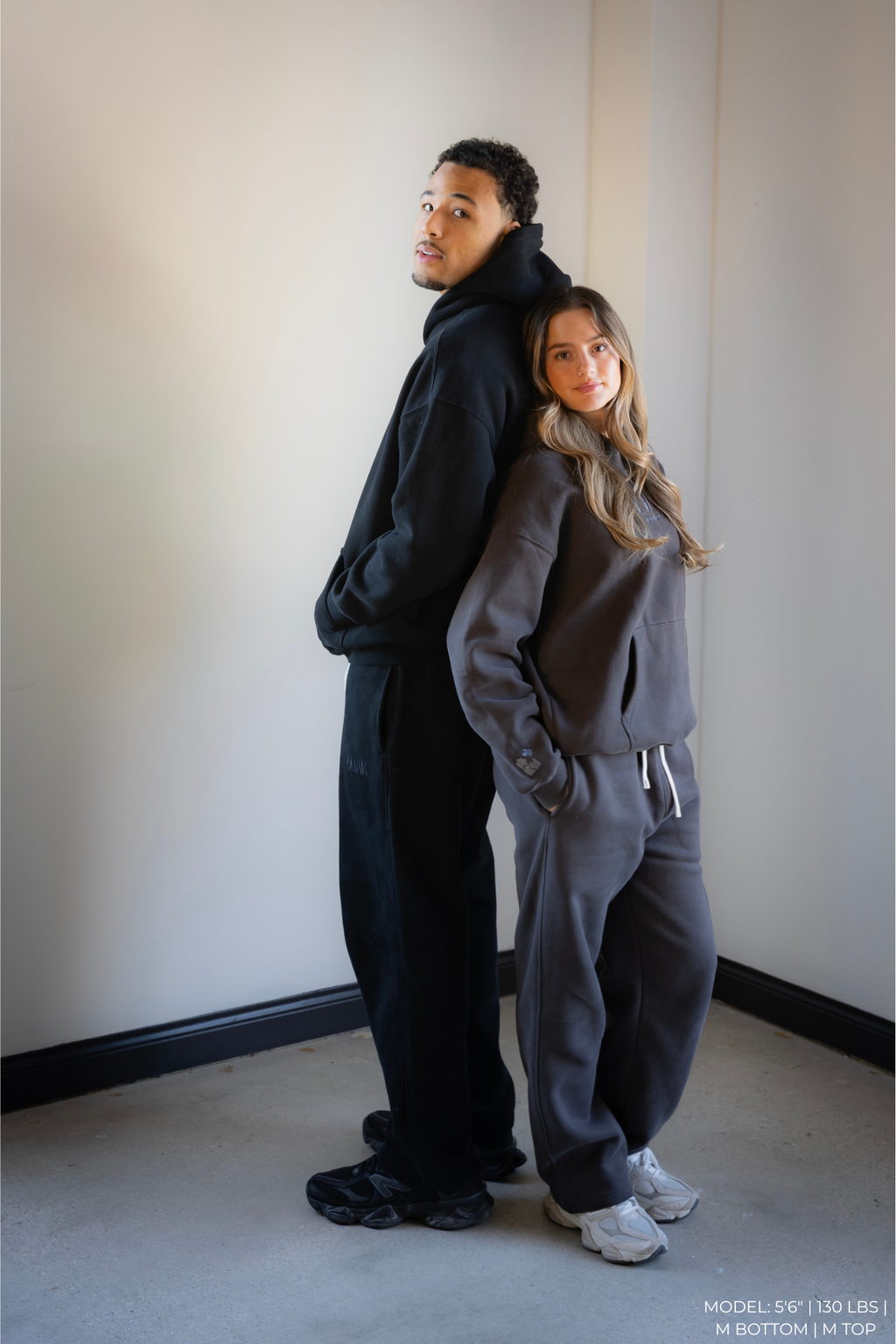 Two models wearing matching dark gray OOAK sets standing against a plain wall.