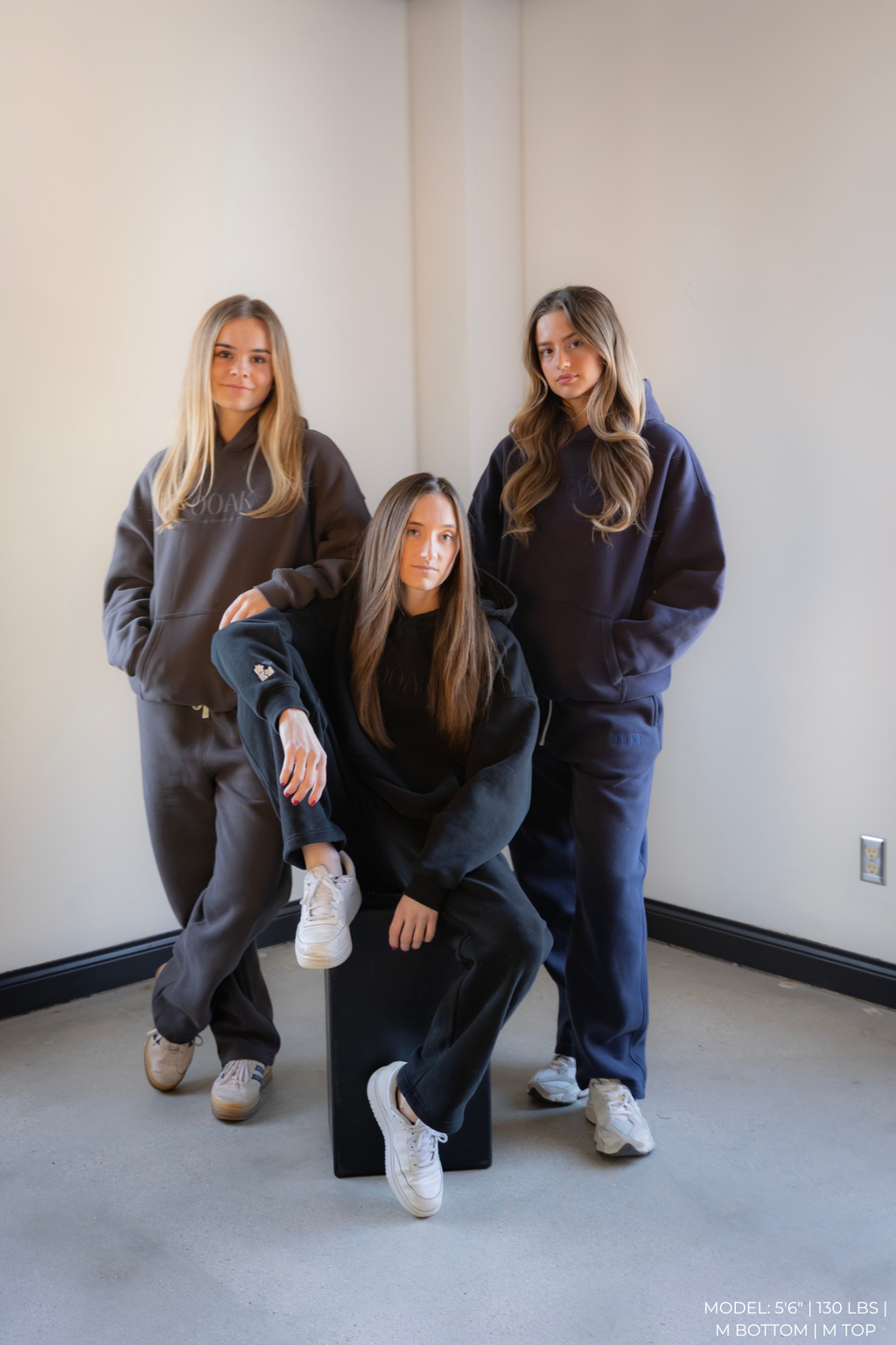 Three women wearing matching dark-colored OOAK sets in a minimal indoor setting.