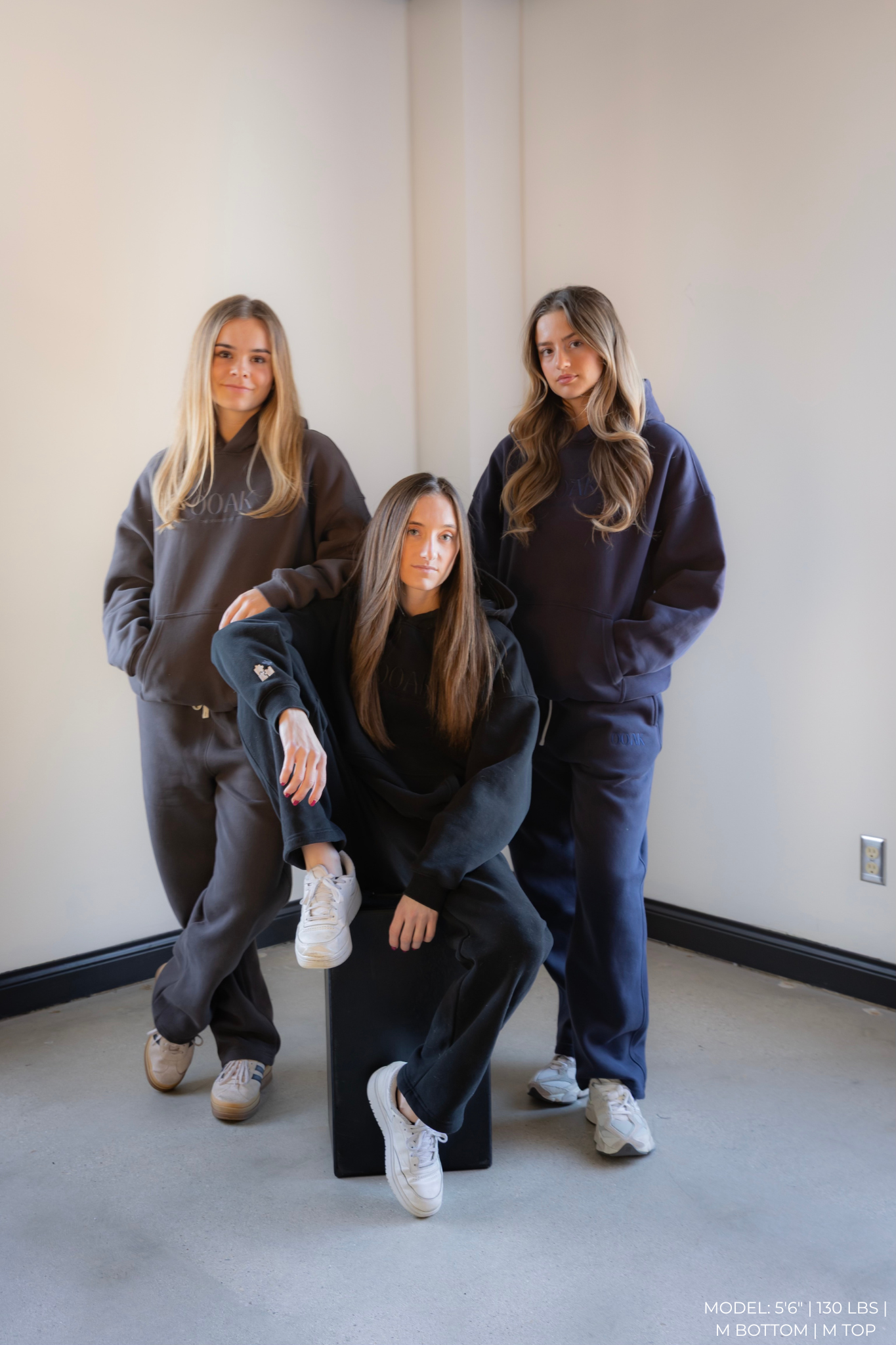 Three women wearing matching dark-colored OOAK sets in a minimal indoor setting.