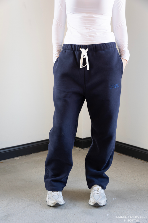 Model wearing navy blue OOAK sweatpants with a white top and white sneakers on a plain background